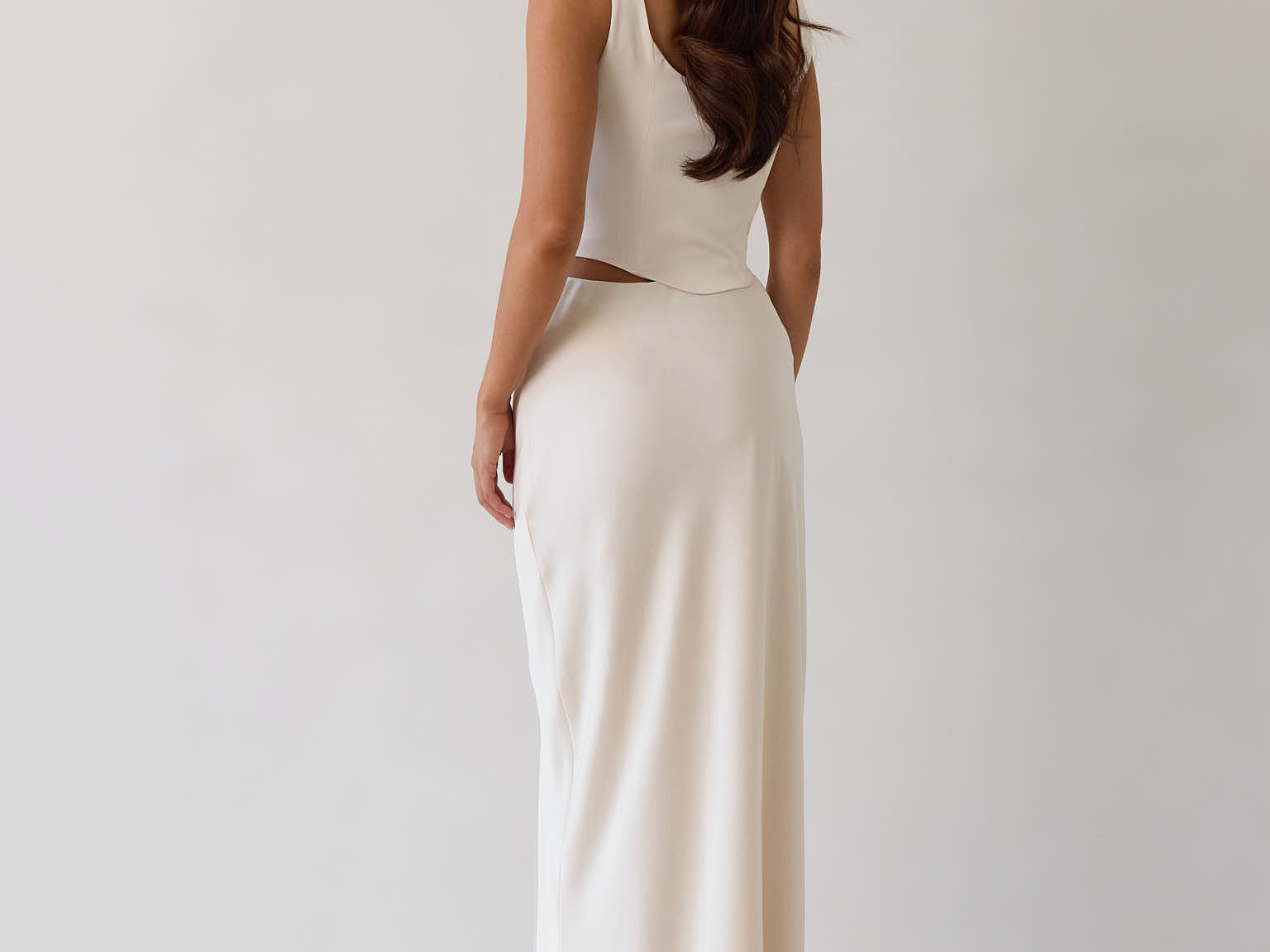 This is the Conrad Set in Ivory. This is a two piece satin set with a fitted, corseted top with thick straps and a delicate tie at the bust and a slight basque waist. It comes with a floor length satin column skirt. 