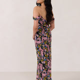 A woman is standing in front of a white background facing the back. She's wearing a bold pink and blue floral print strapless dress with an off-the-shoulder strap. This dress is Sutton in Liora and is perfect as a wedding guest dress, or for any special event. 