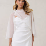A woman is standing against a white backdrop. She's wearing a white bridal dress with a chiffon cape over her shoulders. The cape is gathered slightly on the left side and is nearly fingertip length. This is the Cleo Cape.