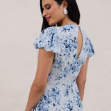 A woman is wearing the Beatrice Dress in Lila. This is a light blue dress with a beautiful blue floral print. The dress has a slightly puffed sleeve, and a full back with a keyhole detail. This is a bra-friendly dress. 
