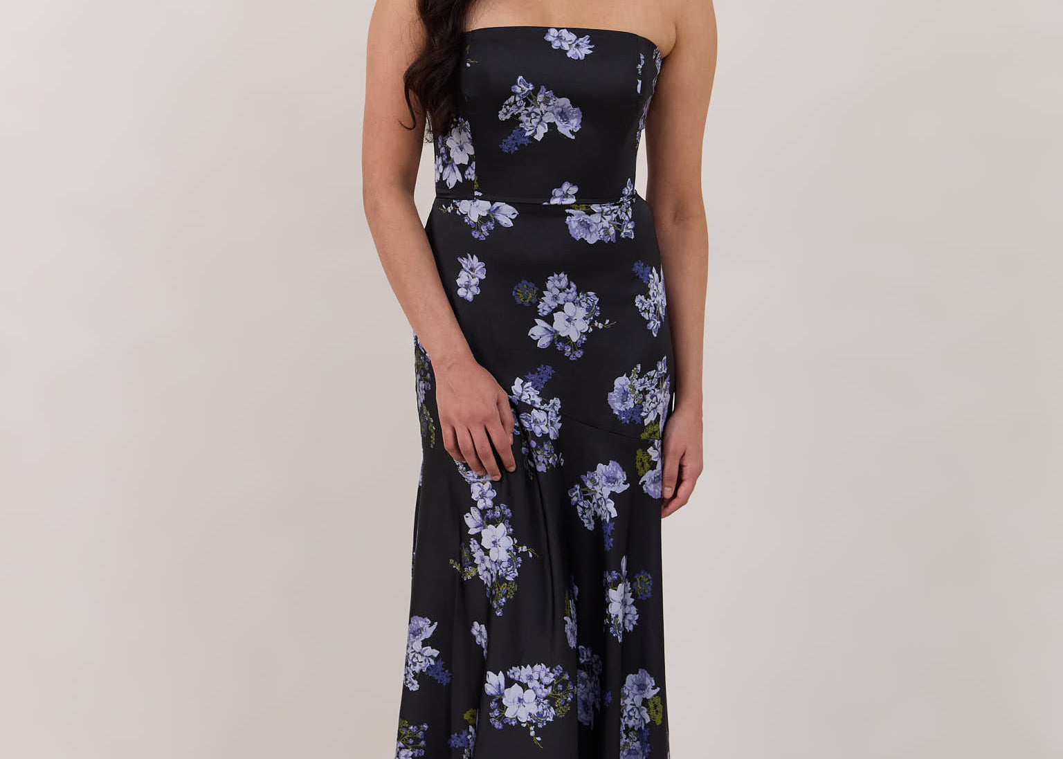 A woman is wearing a dark blue strapless dress with a light blue floral print. The dress is fitted in the bodice and hip then flows into a fuller skirt. The dress is tea-length. This is the Sterling Dress in Viola. 