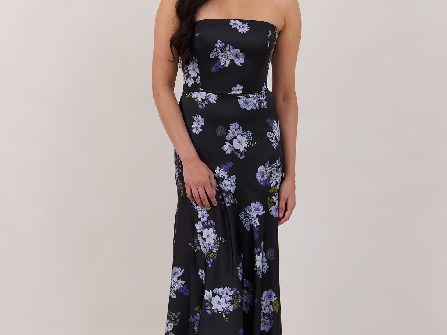 A woman is wearing a dark blue strapless dress with a light blue floral print. The dress is fitted in the bodice and hip then flows into a fuller skirt. The dress is tea-length. This is the Sterling Dress in Viola. 