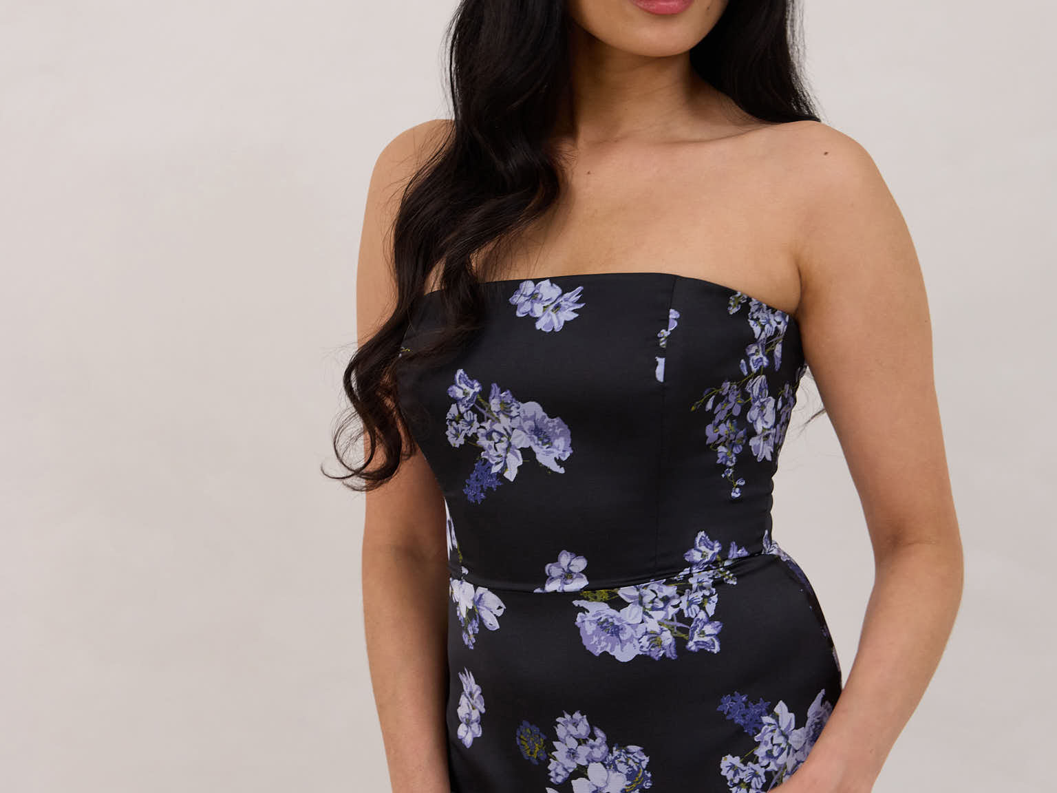 A woman is wearing a dark blue strapless dress with a light blue floral print. The dress is fitted in the bodice and hip then flows into a fuller skirt. The dress is tea-length. This is the Sterling Dress in Viola. 