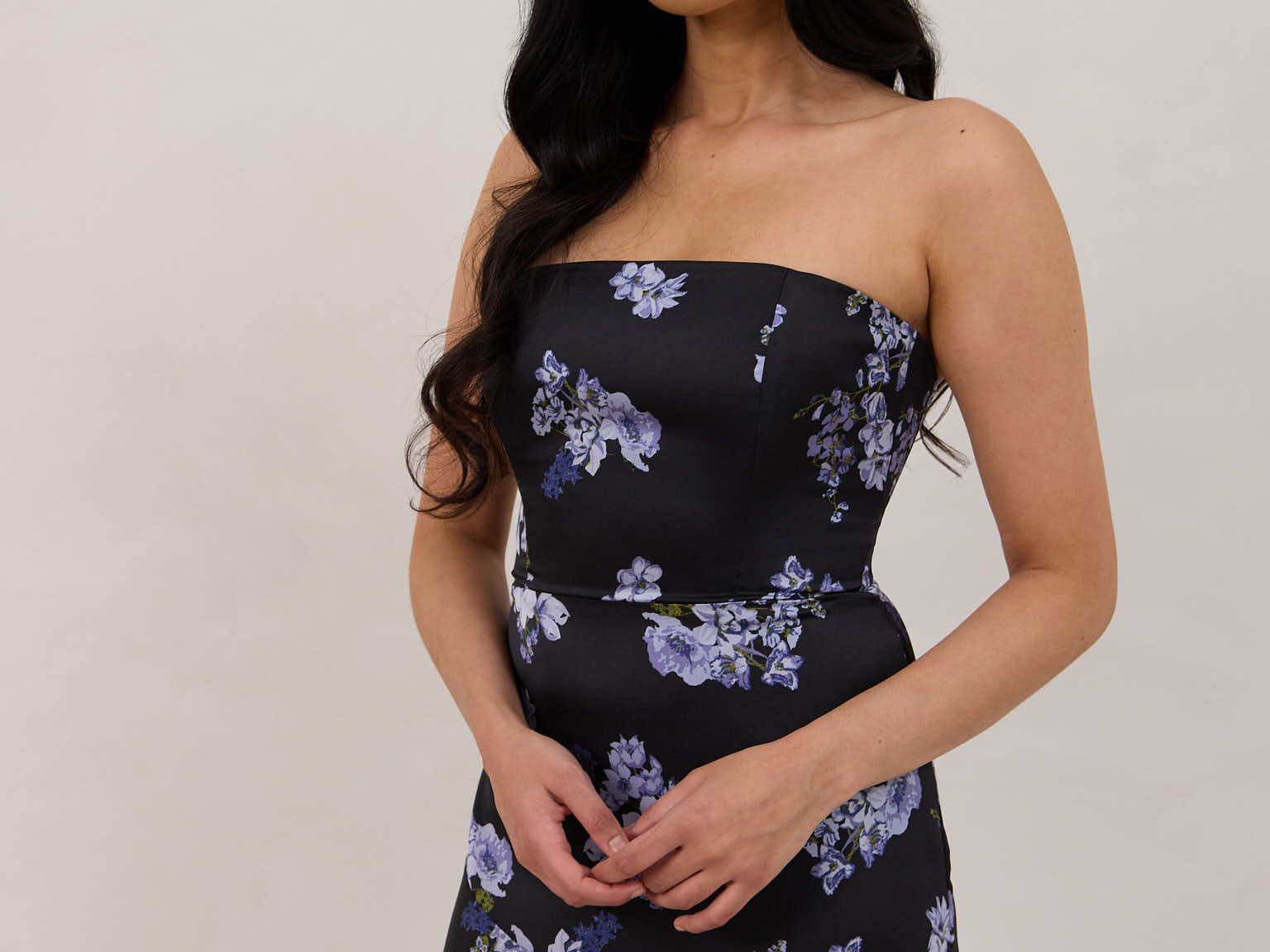 A woman is wearing a dark blue strapless dress with a light blue floral print. The dress is fitted in the bodice and hip then flows into a fuller skirt. The dress is tea-length. This is the Sterling Dress in Viola. 