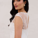 A woman stands against a white backdrop. She's wearing a delicate lace overlay dress on top of a simple white strapless mini bridal dress. This is the Winslow Overlay. 