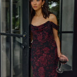 Woman in a dark floral dress holding a glass of red wine, standing in a doorway.