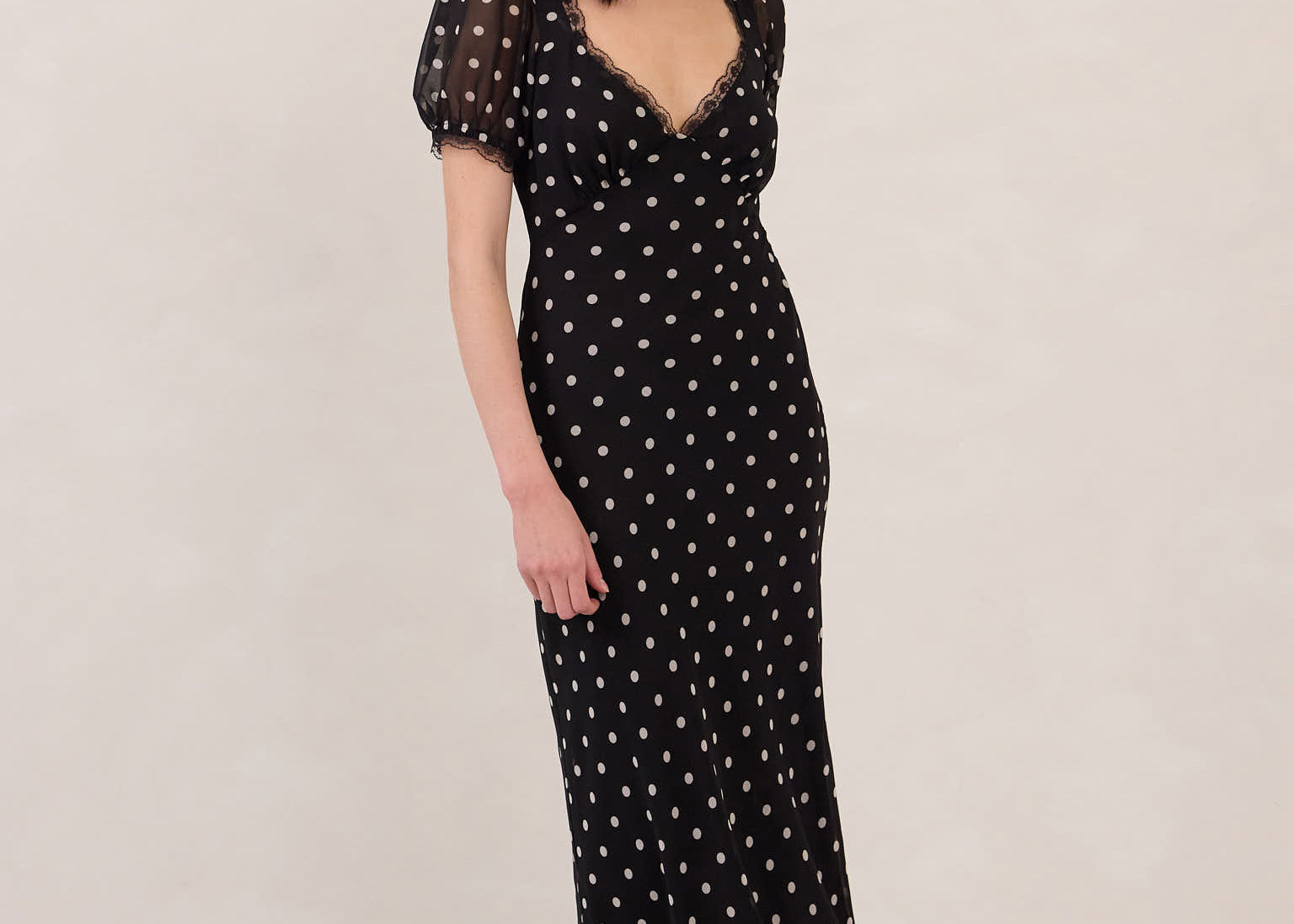 Woman wearing a black dress with white polka dots on a plain background
