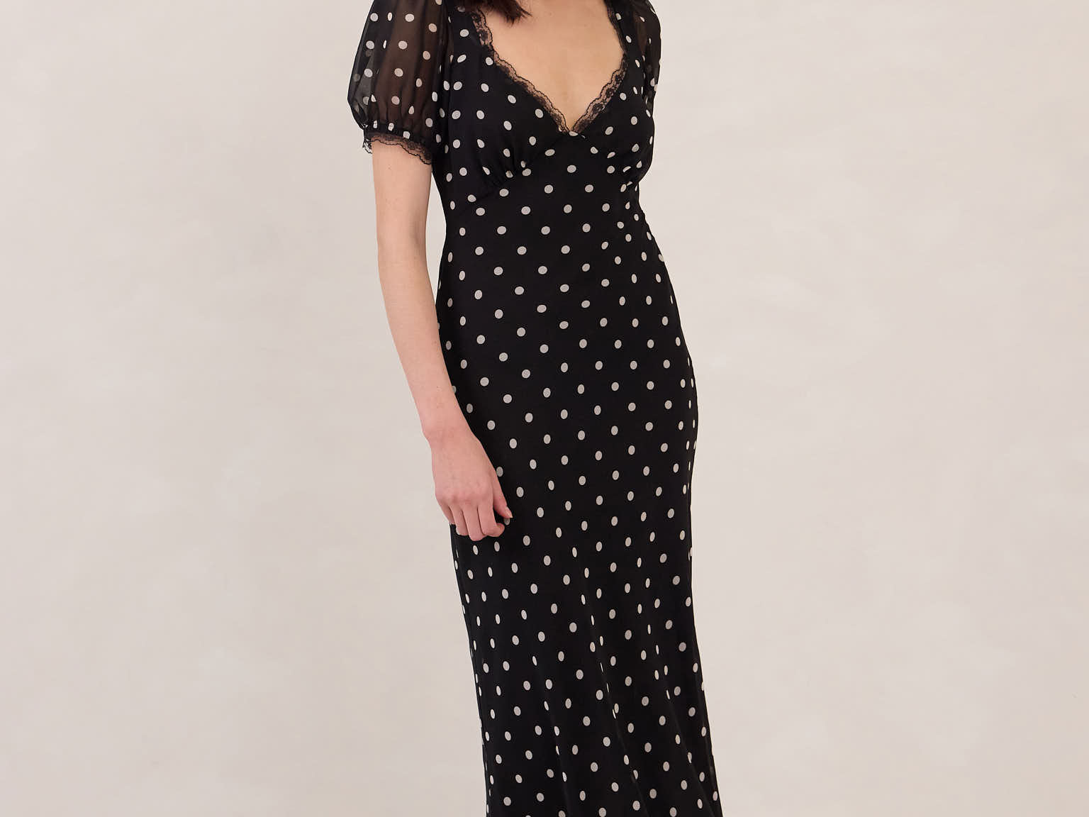 Woman wearing a black dress with white polka dots on a plain background