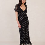 Woman wearing a black dress with white polka dots on a plain background