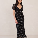 Woman wearing a black dress with white polka dots on a plain background