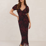 Woman wearing a burgundy floral dress with lace detail on a white background.