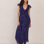 Woman wearing a blue floral dress with a boots and standing against a plain background