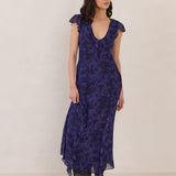 Woman wearing a blue floral dress with a boots and standing against a plain background