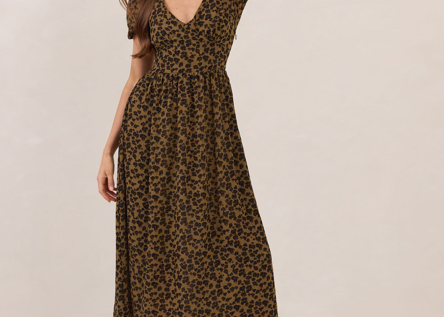 Woman wearing a leopard print dress with black boots on a plain background