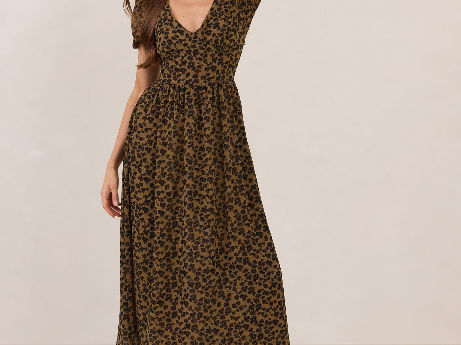 Woman wearing a leopard print dress with black boots on a plain background