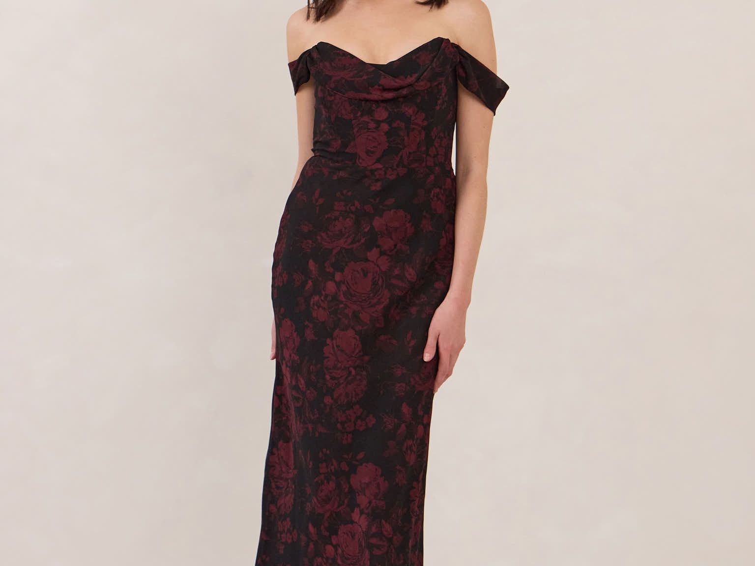 Woman wearing a black and dark red floral off-shoulder gown on a white background