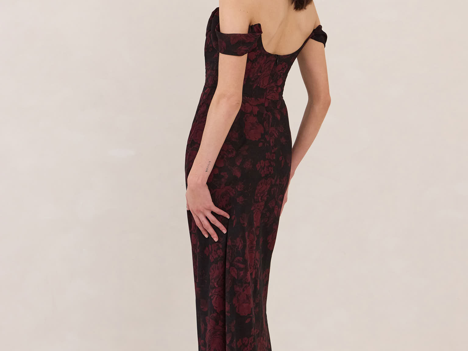 Woman wearing a black and dark red floral off-shoulder gown on a white background