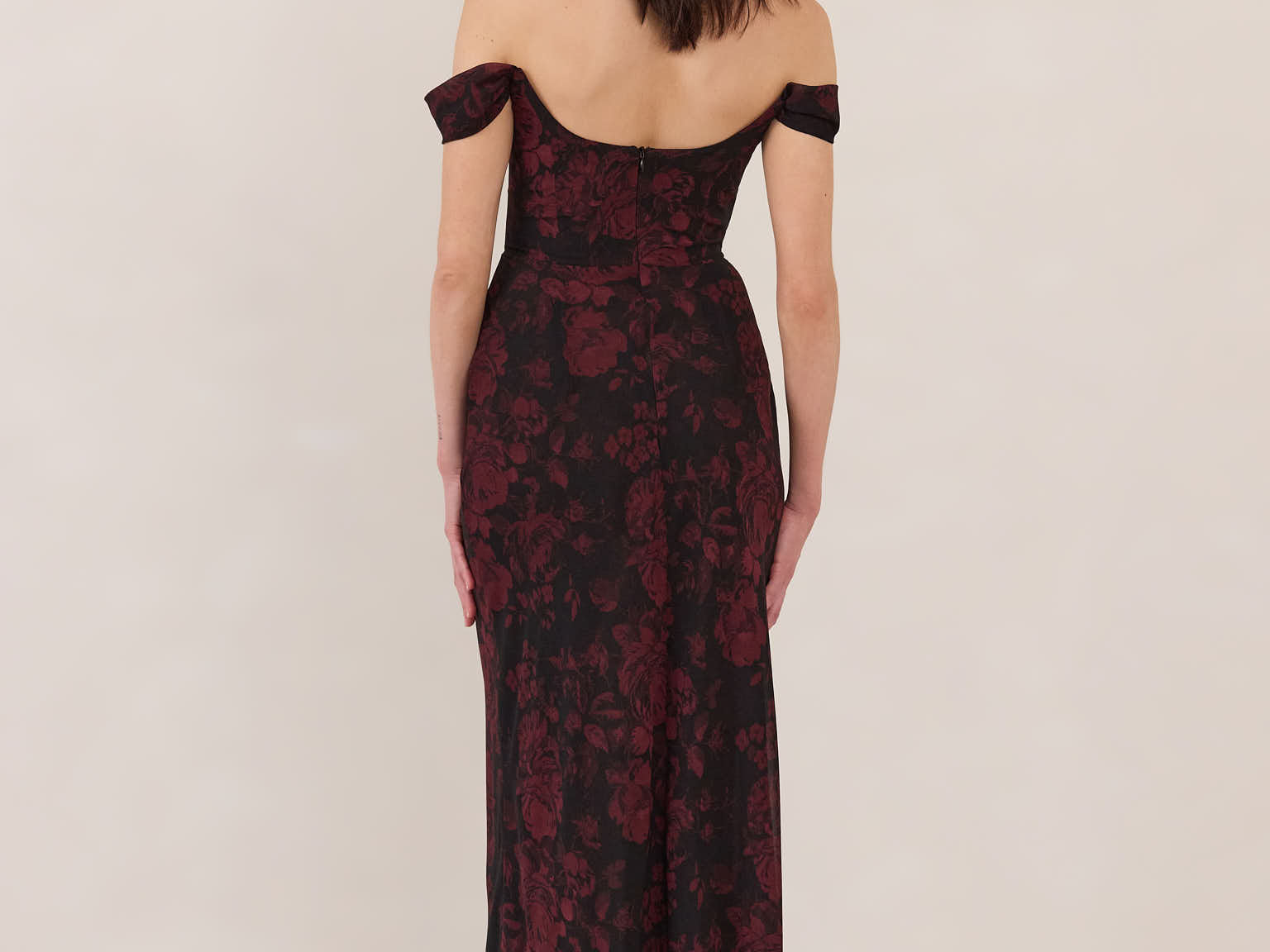 Woman wearing a black and dark red floral off-shoulder gown on a white background