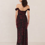 Woman wearing a black and dark red floral off-shoulder gown on a white background
