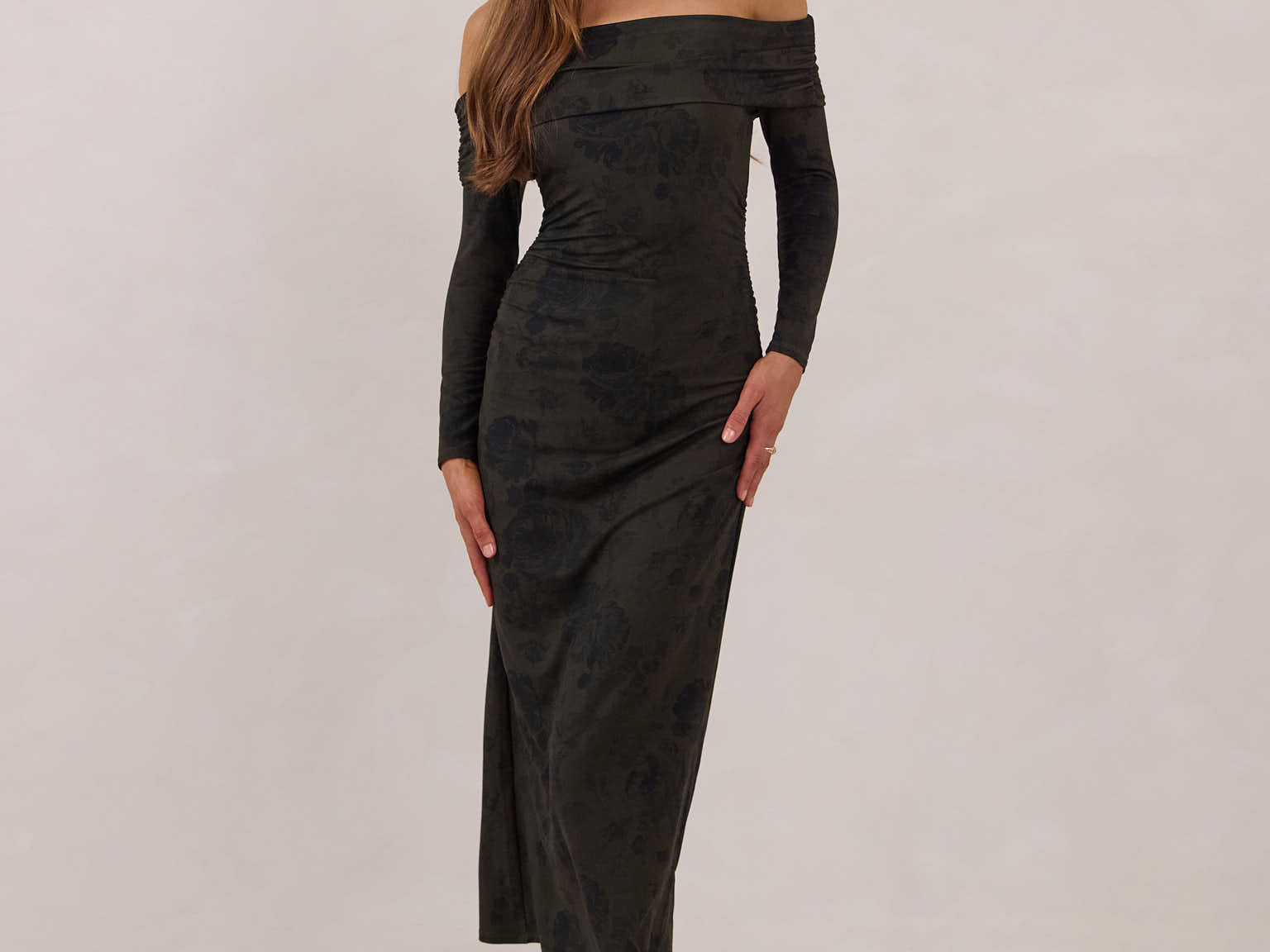Woman wearing a dark olive floral off the shoulder dress standing against a white background