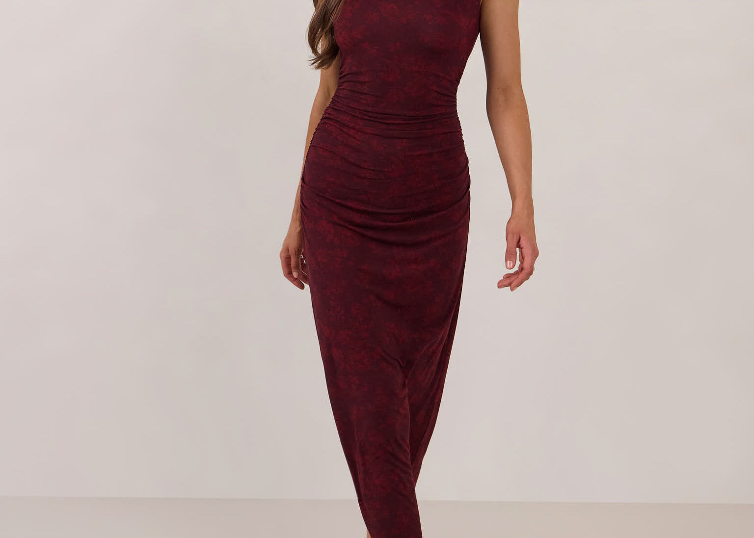 Woman wearing a burgundy floral dress standing against a white background