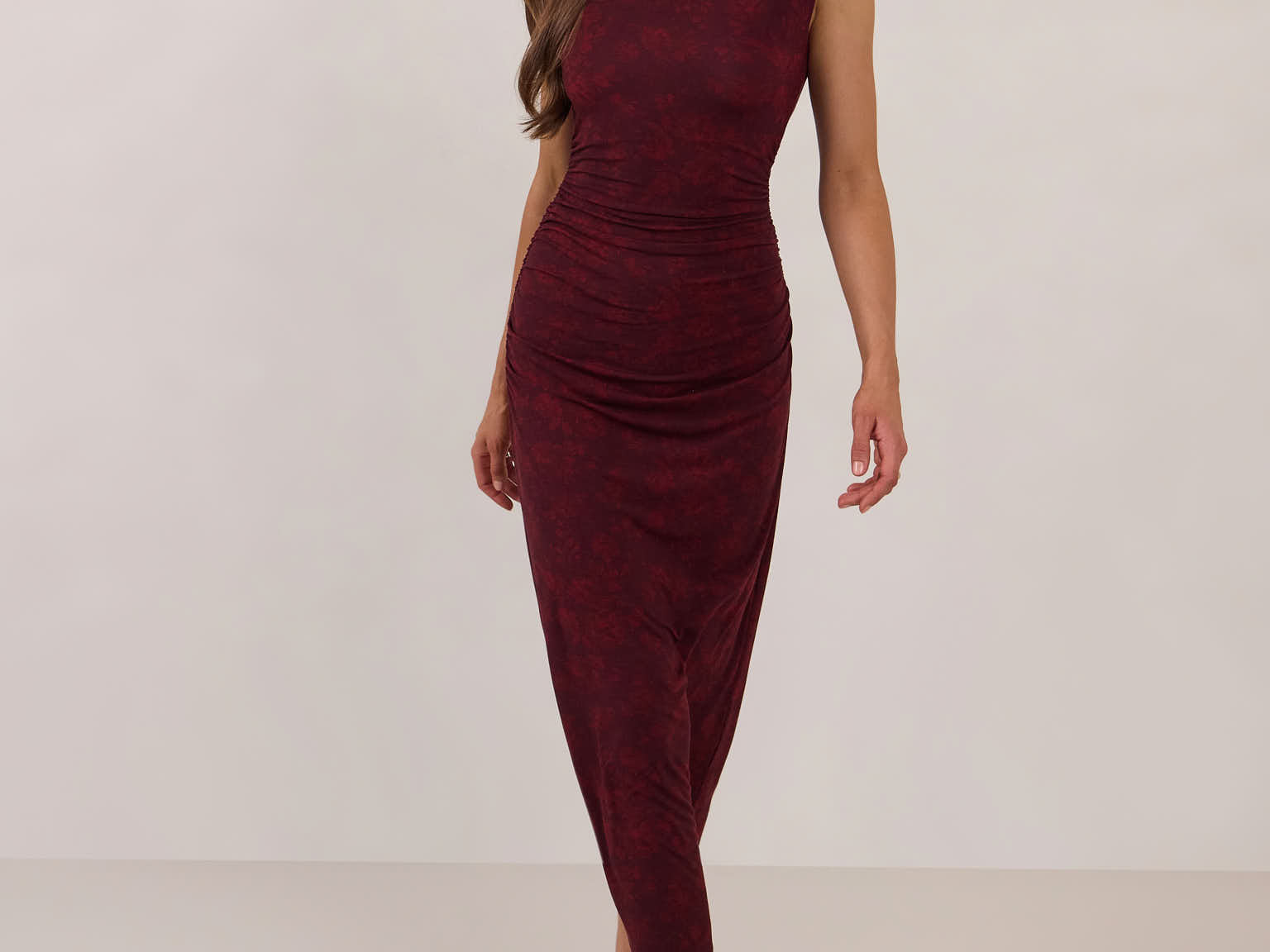 Woman wearing a burgundy floral dress standing against a white background