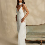 Woman in a white gown standing against a beige background with a vintage couch.