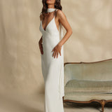 Woman in a white gown standing against a beige background with a vintage couch.