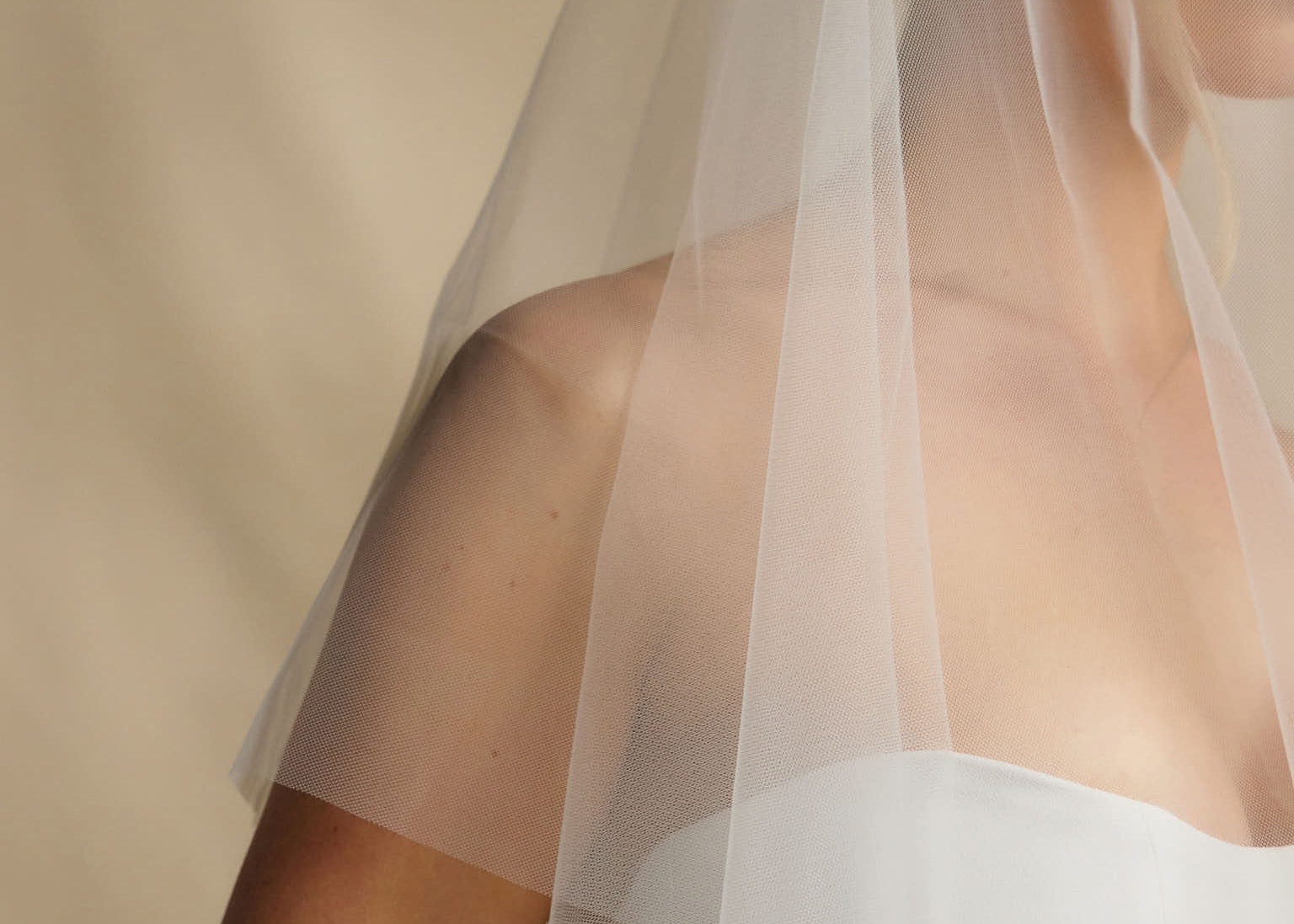 Woman wearing a white wedding dress with a sheer veil against a beige background