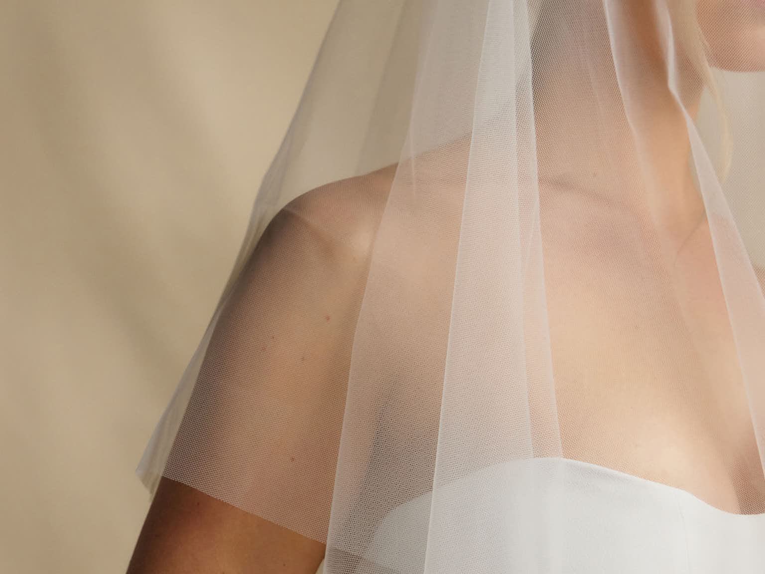Woman wearing a white wedding dress with a sheer veil against a beige background