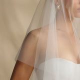 Woman wearing a white wedding dress with a sheer veil against a beige background