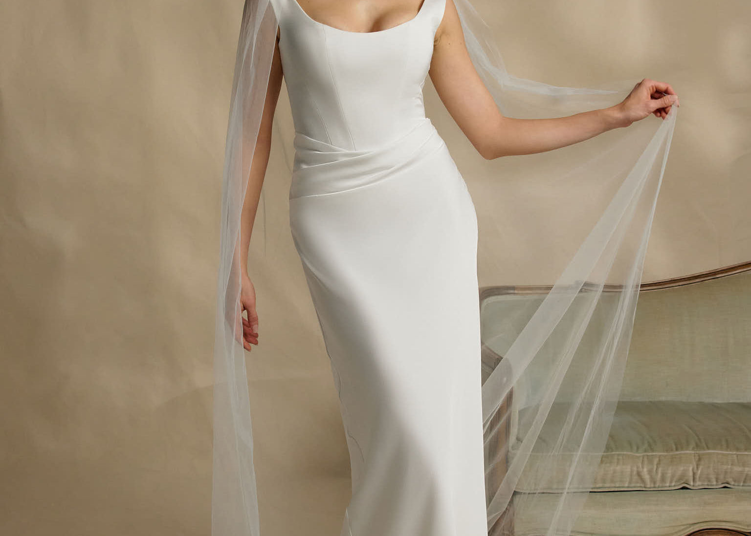 Woman in a white wedding dress with a long veil against a neutral background