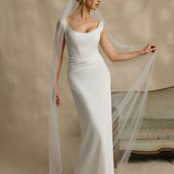 Woman in a white wedding dress with a long veil against a neutral background