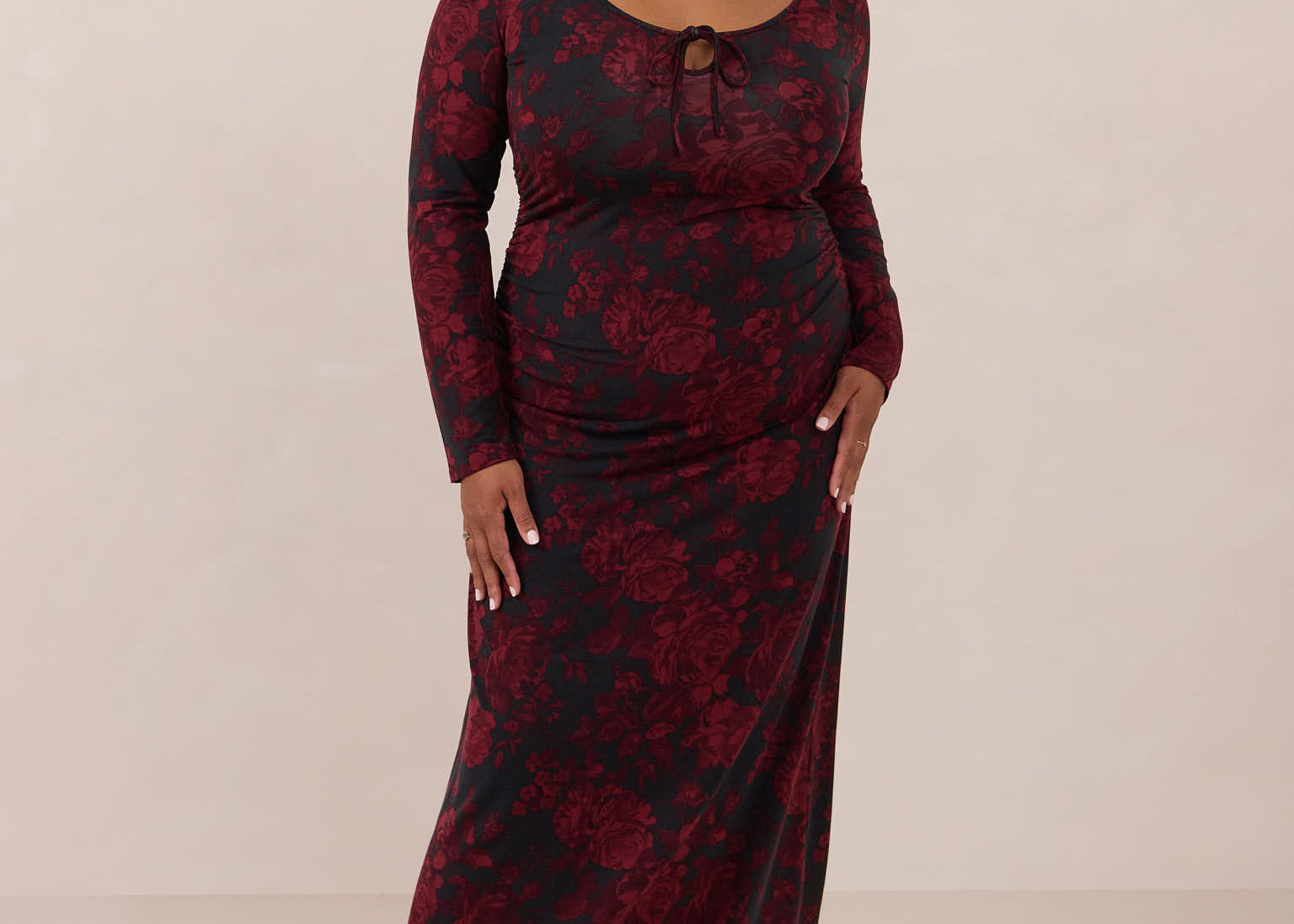 Woman wearing a burgundy floral dress with long sleeves on a beige background