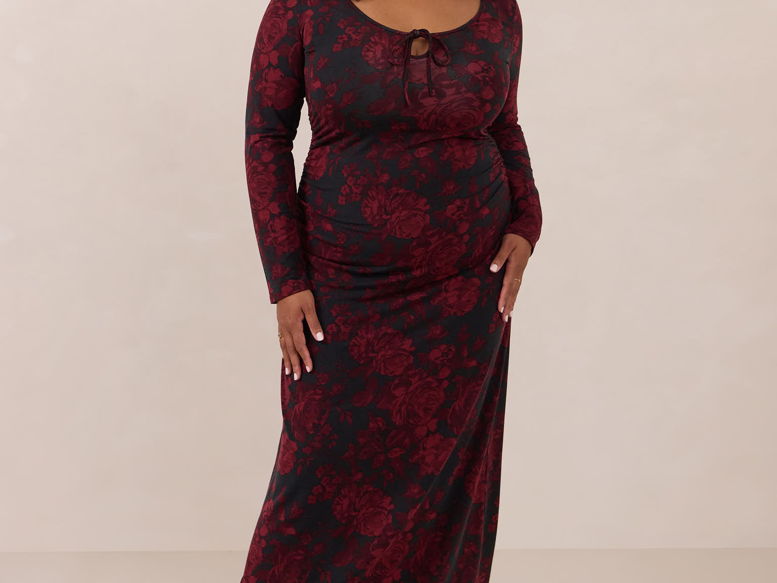 Woman wearing a burgundy floral dress with long sleeves on a beige background