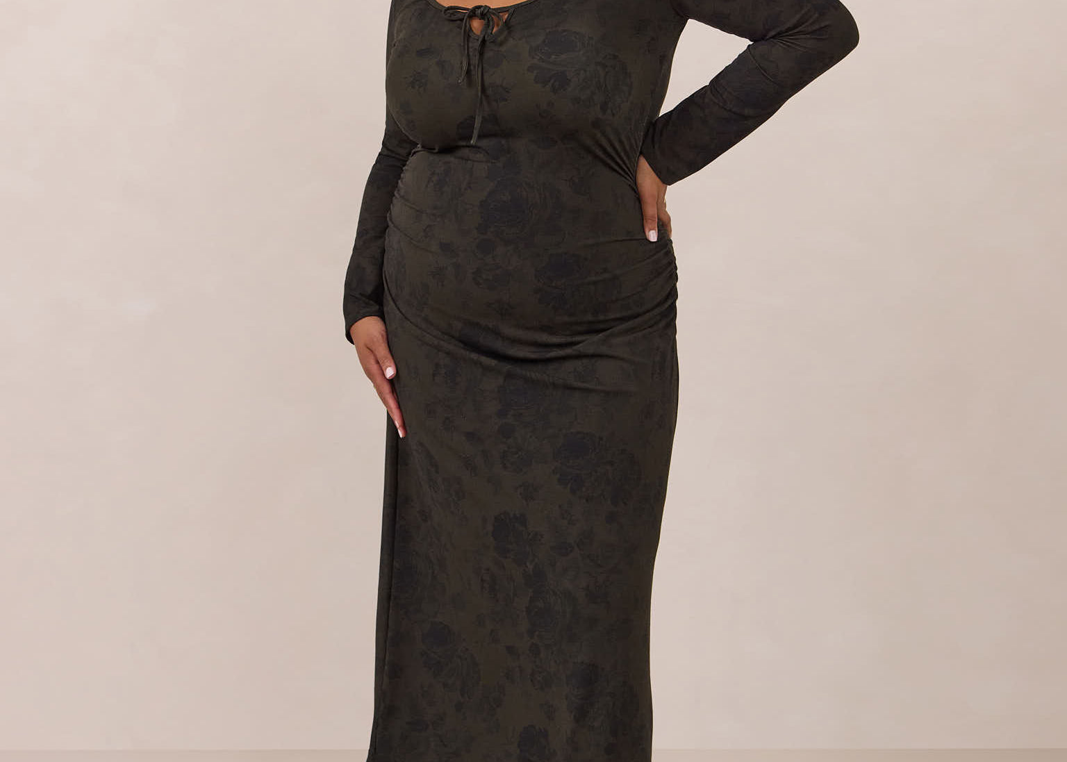 Woman wearing a dark olive floral patterned dress standing against a plain background