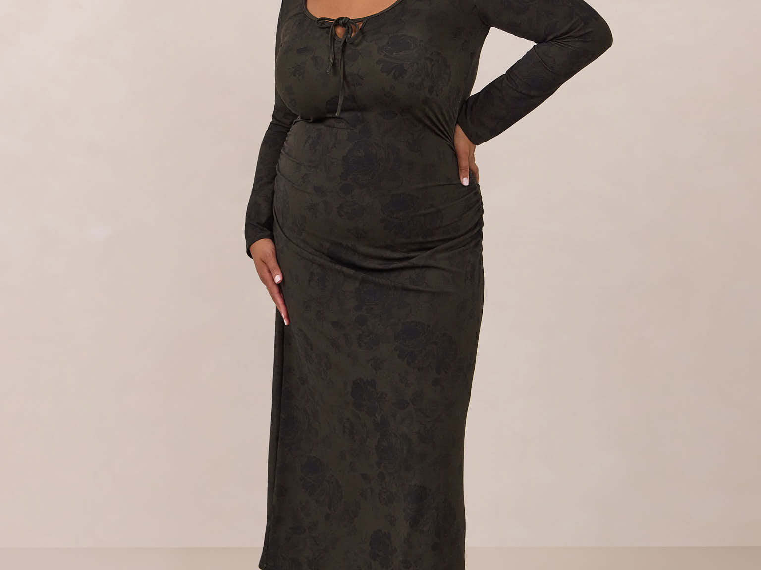 Woman wearing a dark olive floral patterned dress standing against a plain background
