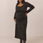 Woman wearing a dark olive floral patterned dress standing against a plain background