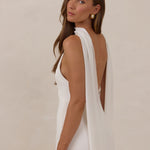 Woman wearing a white dress and chiffon scarf with a low back against a beige background