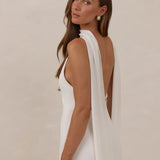 Woman wearing a white dress and chiffon scarf with a low back against a beige background