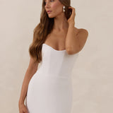 Woman wearing a white strapless dress against a beige background