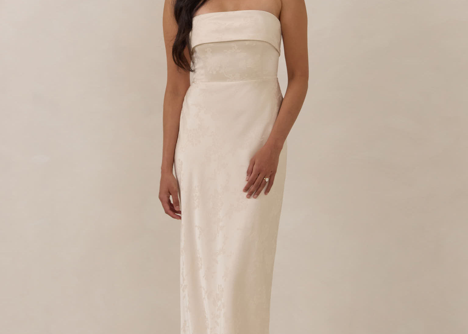 Woman wearing a strapless ivory dress standing against a plain background