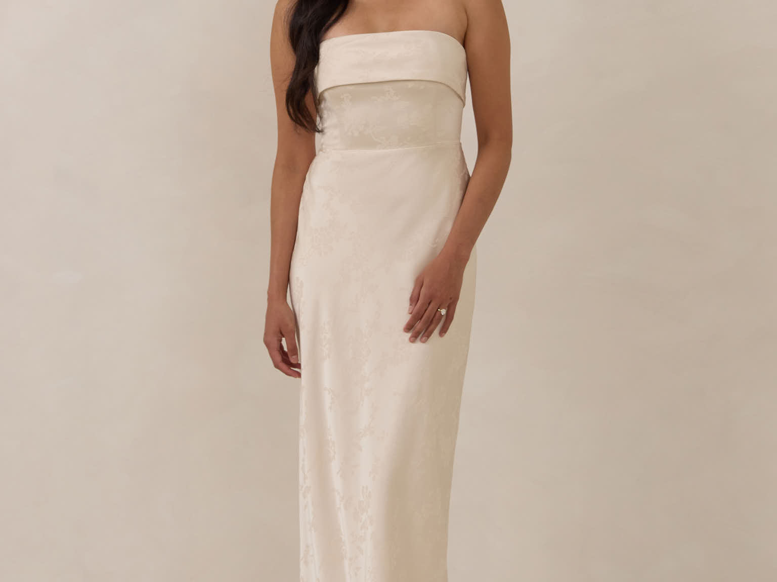 Woman wearing a strapless ivory dress standing against a plain background