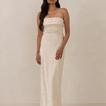 Woman wearing a strapless ivory dress standing against a plain background