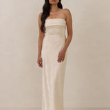 Woman wearing a strapless ivory dress standing against a plain background