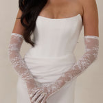 Woman wearing a white strapless dress with lace gloves against a neutral background