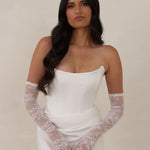 Woman wearing a white strapless dress with lace gloves against a plain background
