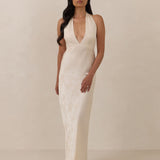 Woman wearing a ivory halter neck dress standing against a plain background