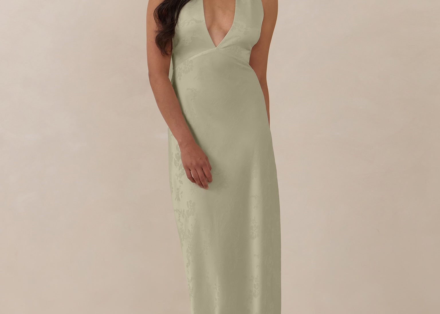 Woman wearing a true sage halter neck dress in jacquard fabric standing  against a beige background