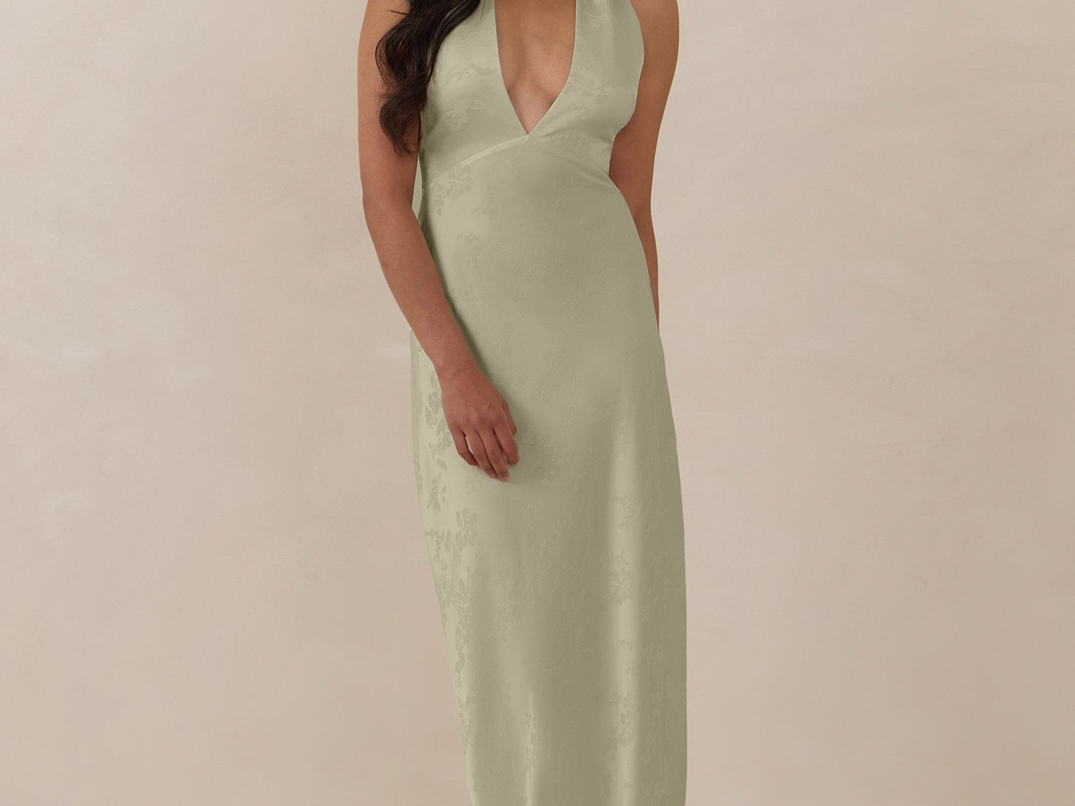 Woman wearing a true sage halter neck dress in jacquard fabric standing  against a beige background